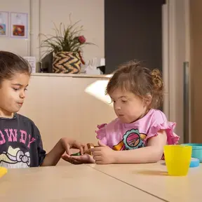 Twee leerlingen met hoortoestellen delen iets aan tafel.