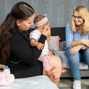 Een ambulant behandelaar doet een hoortoestel in bij een baby, terwijl een moeder toekijkt