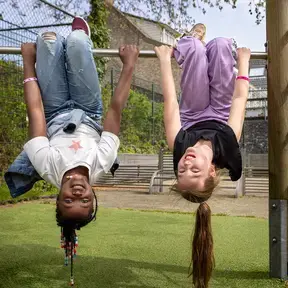 Twee kinderen hangen ondersteboven aan een klimrek en lachen.
