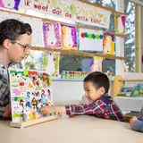 Leerkracht werkt met twee jongens aan een taaloefening met een prentenboek.