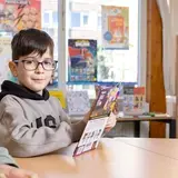 Jongen met bril leest een boek in de schoolbibliotheek.