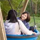 Twee meisjes schommelen samen lachend in een nestschommel.