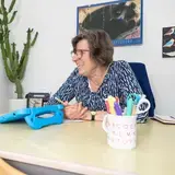 Leerkracht en leerling werken lachend samen aan een tafel met tablet.