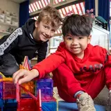 Twee jongens bouwen lachend samen met magnetische bouwstenen.