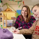 Leerkracht werkt met twee kinderen aan een taal- of spraakoefening met beeldkaarten.