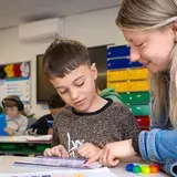 Leerkracht helpt een leerling individueel bij een schrijfopdracht in de klas.