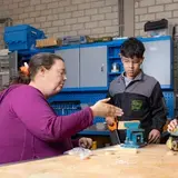 Een docent begeleidt twee leerlingen bij een technische opdracht in een werkplaats.
