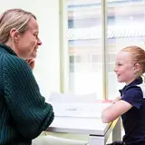 Een therapeut praat met een kind dat een hoortoestel draagt.