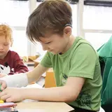 Een leerling met hoortoestel schrijft aan zijn tafel in de klas.