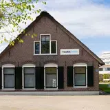Vooraanzicht van locatie met een puntdak en een bord met Auris Zorg