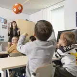 Leerkracht gooit een bal met rekentekens terwijl een groep leerlingen reageert in de klas.
