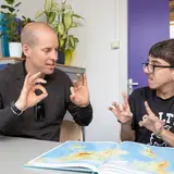 Een docent en een leerling gebruiken gebarentaal terwijl ze een atlas bekijken.