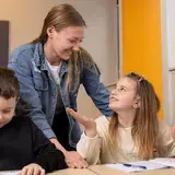 Leerkracht helpt twee leerlingen met schrijven in de klas.