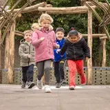 Vier leerlingen rennen lachend door een houten tunnel op het schoolplein.