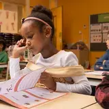 Een leerling leest een werkboek in de klas.