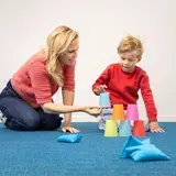 Een leerling bouwt een piramide van gekleurde bekers, met een begeleider ernaast.