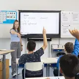 Leerkracht bespreekt een dictee met de klas, leerlingen steken hun vinger op
