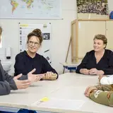 Vijf collega's overleggen aan tafel in een klaslokaal