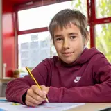 Een leerling schrijft aan zijn tafel in de klas.