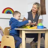 Begeleider helpt een jong kind met het snijden van groente aan een tafeltje