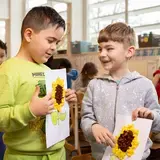 Twee leerlingen laten elkaar hun knutselwerk van een zonnebloem zien.