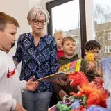 Een begeleider laat een boek en speelgoeddinosaurussen zien aan een groep leerlingen.