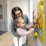 Een vrouw helpt een peuter met een kleurrijk wandspeelgoed met een giraffe.Een vrouw helpt een peuter met een kleurrijk wandspeelgoed met een giraffe.