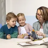 Een vrouw laat twee kinderen een knuffeldier en een prentenboek zien.