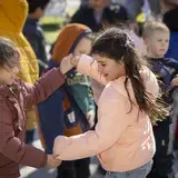 Twee meisjes stoten hun ellebogen tegen elkaar buiten, tussen andere kinderen.