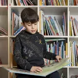 Een jongen leest een prentenboek voor een boekenkast met kinderboeken.
