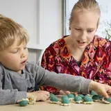 Een logopedist en een jongen leggen samen gehaakte schildpadjes op een rij.