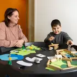 Leerkracht kijkt toe terwijl een leerling op de speeltafel met letterkaartjes en figuurtjes speelt.