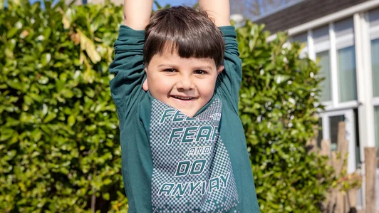 Lachende jongen met armen omhoog op het schoolplein.