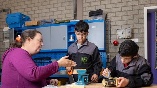 Een docent begeleidt twee leerlingen bij een technische opdracht in een werkplaats.