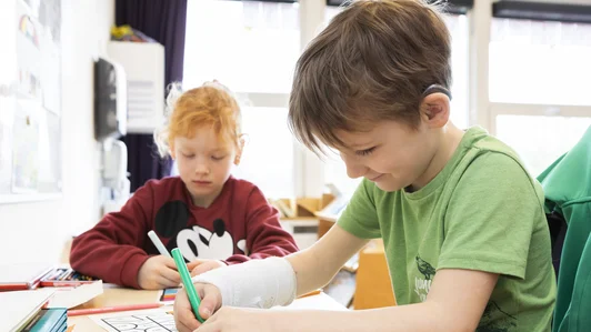 Een leerling met hoortoestel schrijft aan zijn tafel in de klas.