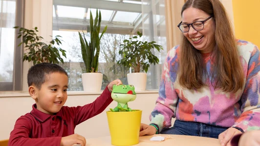 Een begeleider laat een pluchen kikker zien aan een leerling tijdens een taaloefening.