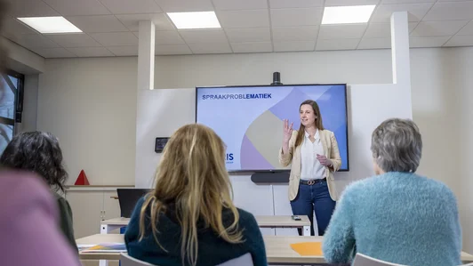 Een vrouw geeft een presentatie over spraakproblematiek voor een groep collega's.