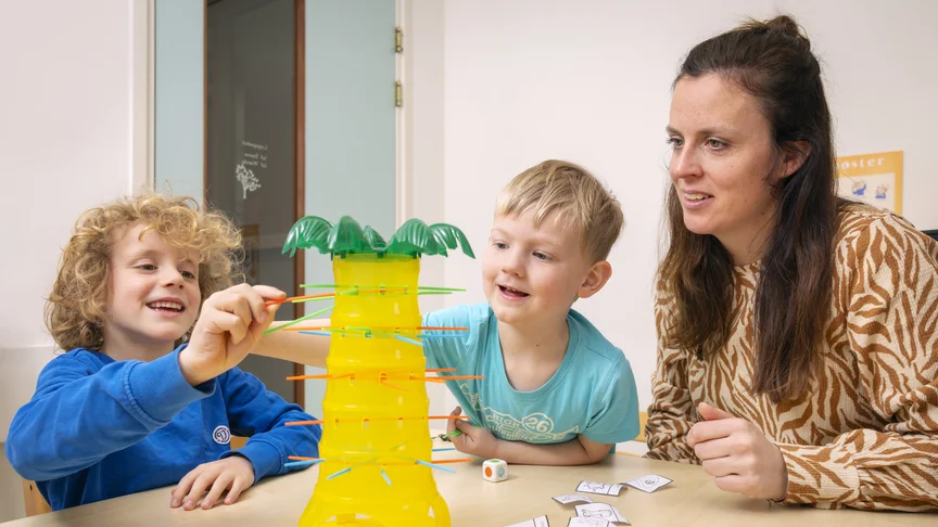 Twee kinderen spelen een spel. Volwassene kijkt toe.