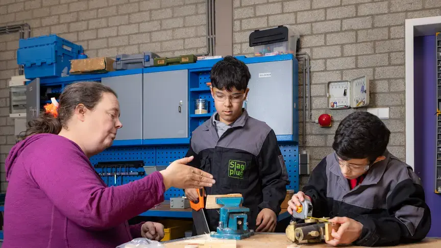 Een docent begeleidt twee leerlingen bij een technische opdracht in een werkplaats.