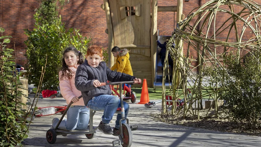 Twee kinderen rijden op een skelter over het schoolplein.