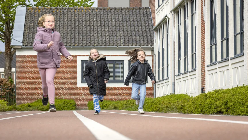 Drie kinderen rennen buiten over een atletiekbaan bij school