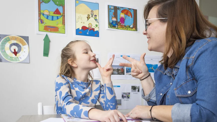 Begeleider en kind doen samen een spraakoefening met handgebaren