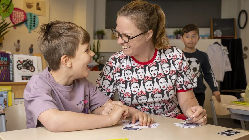 Een leerkracht en een leerling spelen een kaartspel aan tafel. Ze oefenen samen taal.