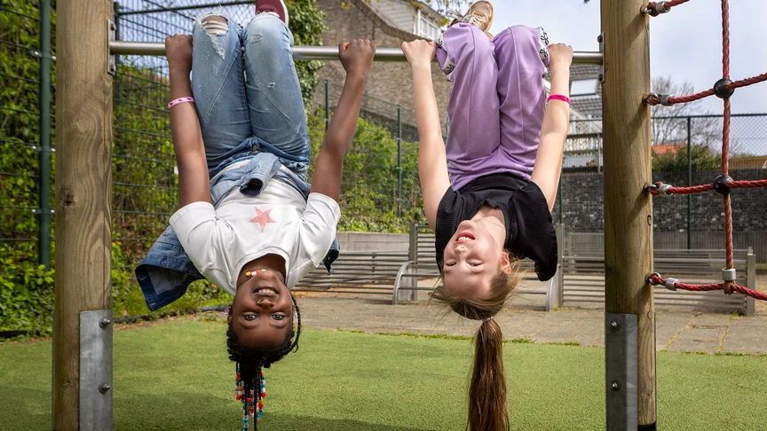 Twee kinderen hangen ondersteboven aan een klimrek en lachen.