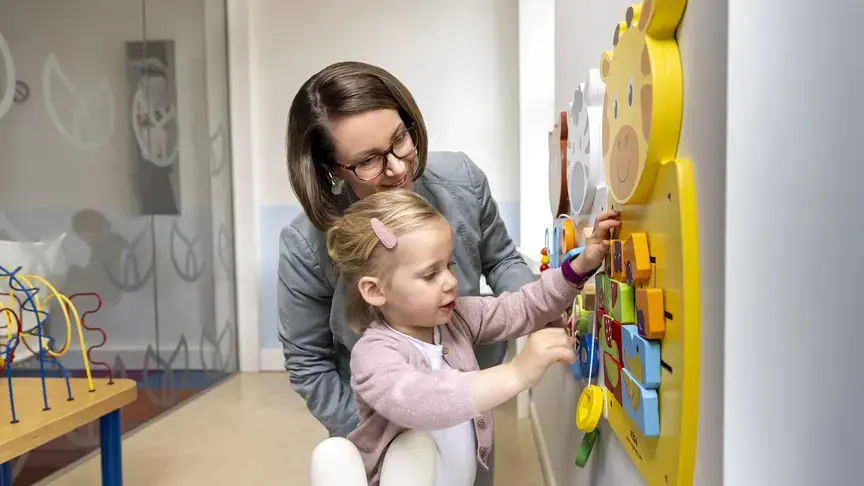 Een vrouw helpt een peuter met een kleurrijk wandspeelgoed met een giraffe.Een vrouw helpt een peuter met een kleurrijk wandspeelgoed met een giraffe.