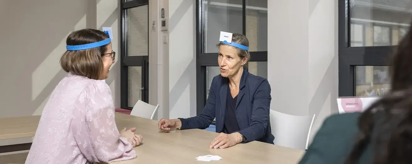 Twee vrouwen doen een raadspel met kaarten op een blauwe hoofdband.