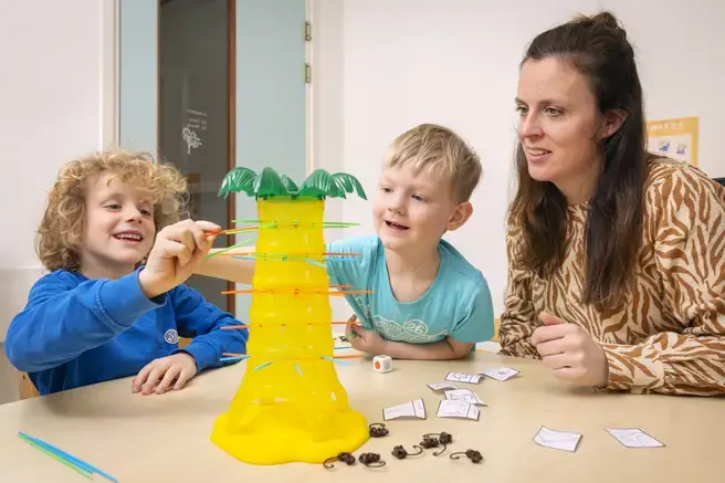Twee kinderen spelen een spel. Volwassene kijkt toe.