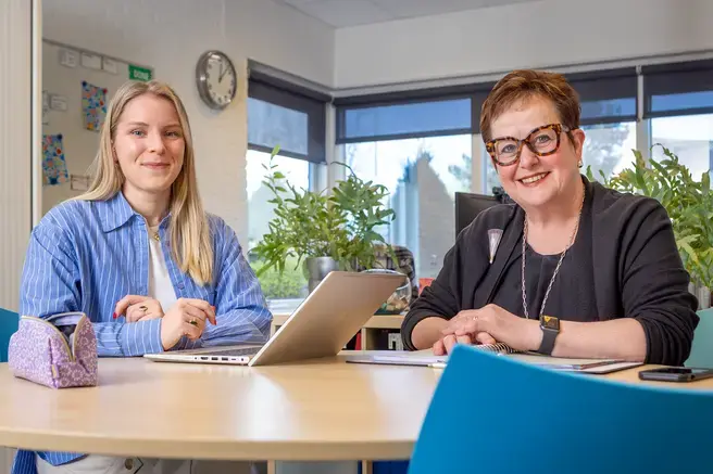 Twee collega's overleggen aan een tafel met laptop.