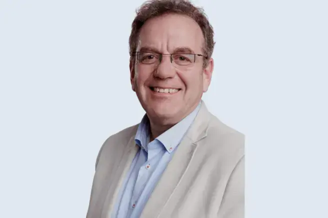 Man met bril en wit jasje aan kijkt in de camera