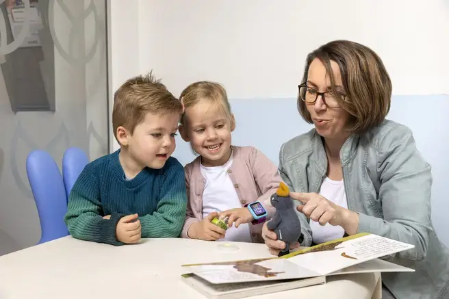 Een vrouw laat twee kinderen een knuffeldier en een prentenboek zien.